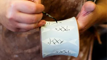 A hand paints a mug with fish motifs.