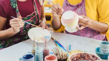 Two people paint crockery together in a studio.