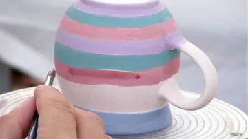 A painted mug is processed with a brush.