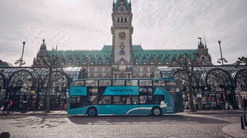 A double-decker bus is parked in front of Hamburg's historic town hall.