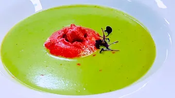 Grüne Suppe mit roter Garnitur und Kräutern in Schüssel.