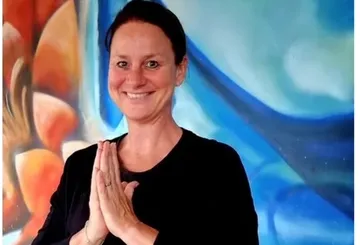 Frau lächelt und faltet die Hände vor einer Malerei.