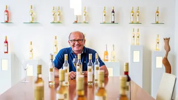 Man sits at a table with bottles of wine in a cozy setting.