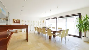 Dining room with bright light, long tables and plants.
