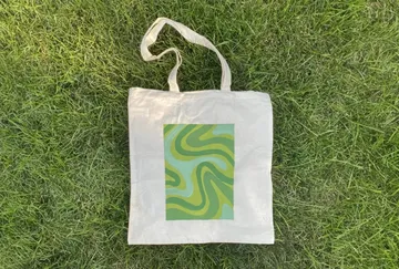 Stofftasche liegt auf grünem Gras mit spiralförmigem Design.