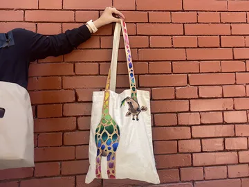 Stofftasche mit Giraffen-Design an roter Ziegelwand.