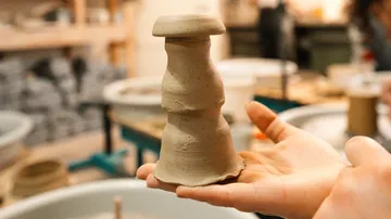 One hand holds an unglazed clay figure in a workshop.