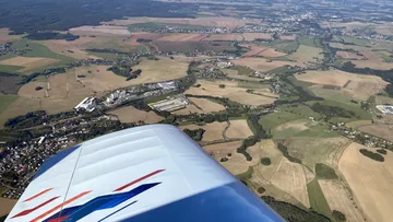 Flugzeugflügel schneidet durch die Luft über landwirtschaftlichen Flächen.