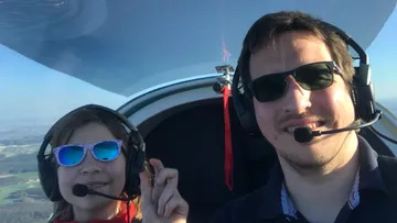 Zwei Personen im Flugzeug lächeln mit Kopfhörern.