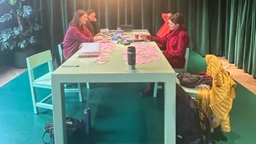 Three women sit at a table and work together.