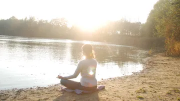 Person meditiert am ruhigen See bei Sonnenlicht.