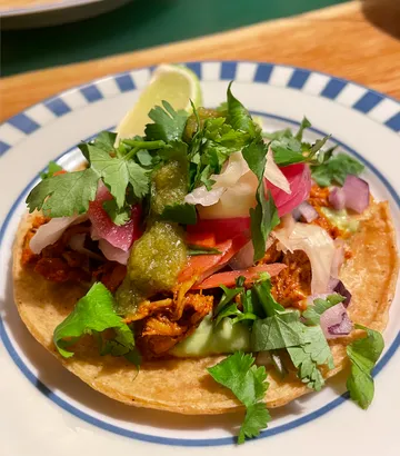 Taco mit Fleisch, Salat und Limette auf Teller.