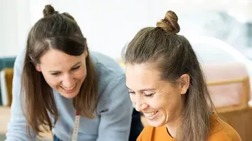 Zwei Frauen lächeln und arbeiten gemeinsam an einem Projekt.