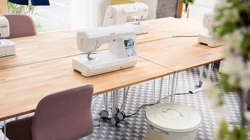 Nähmaschinen stehen auf einem Tisch in einem hellen Raum.