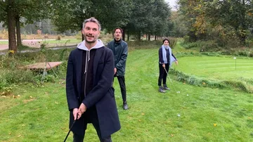 Three people practice golf in the autumnal park.