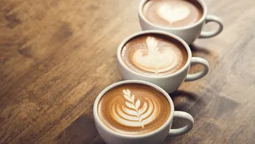 Drei Tassen Kaffee mit schönen Latte-Art-Mustern auf Holzoberfläche.