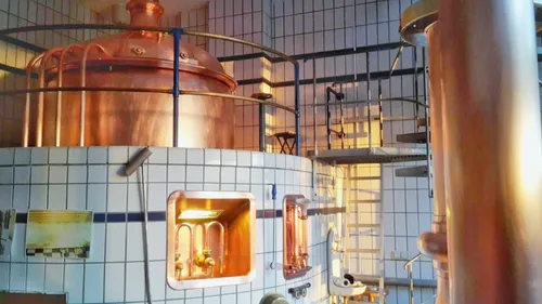 Kupferne Brauanlage in hell erleuchtetem Raum mit Treppe.