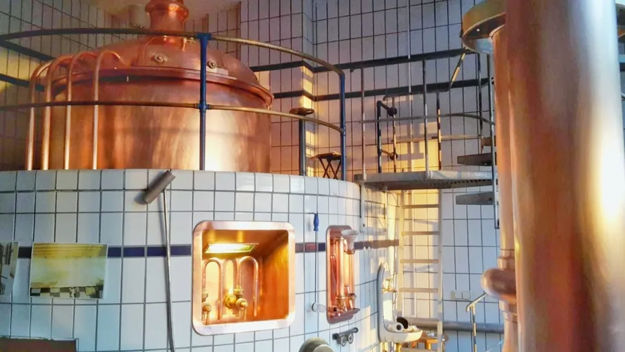 Kupferne Brauanlage in hell erleuchtetem Raum mit Treppe.