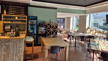 Holzbar mit Getränken, Tischen in hellem Restaurant.