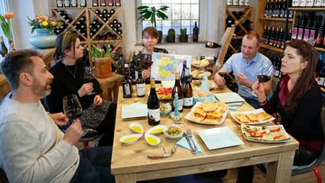 Fünf Personen genießen Wein und Essen in einem Weingeschäft.
