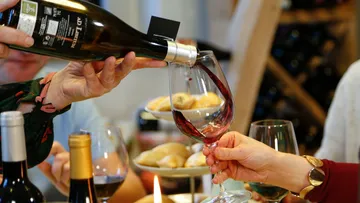 Rotwein wird in ein Glas gegossen, umgeben von Snacks.