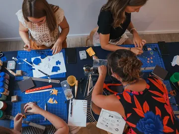 Three women are creatively tinkering on a table full of materials.