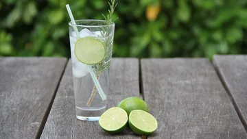 Glass with water, ice, limes and herbs on wood.