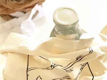 Glasflasche in Tasche auf hellem Tisch mit Gegenständen.