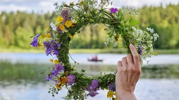 A hand holds a blooming wreath over a lake.