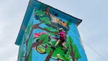 Kletterer erklimmt bunten, bemalten Turm unter einem blauen Himmel.