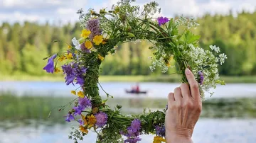 A wreath of flowers is held over a lake by hand.