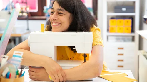 Sewing machine hugged by smiling woman in bright surroundings.