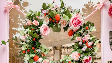 A wreath of flowers decorated with roses hangs on a window.