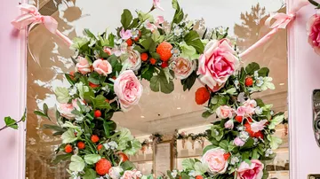 Blumenkranz schmückt eine Fensterfront, umgeben von Pflanzen.