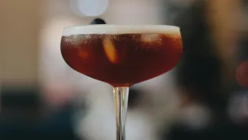 Cocktail glass with dark drink and ice cubes in the background.