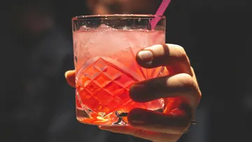 A glass of pink drink is held.