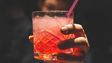 Ein Glas mit pinkem Getränk wird gehalten.