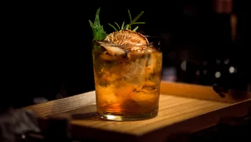 Cocktailglas mit Eis und Dekoration auf Holztablett.