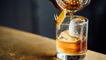 Ein Glas wird mit einem Getränk gefüllt, Eiswürfel vorhanden.