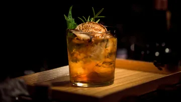 Ein Glas mit Cocktail steht auf einem Holzbrett, dekoriert.
