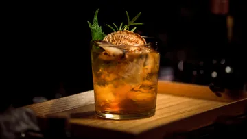 A glass with cocktail is placed on a wooden board.