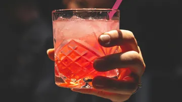 A glass of ice and pink drink is held.