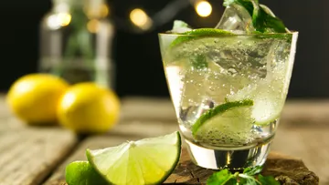 Ein Glas mit Getränk, Limetten und Minze auf Holz.