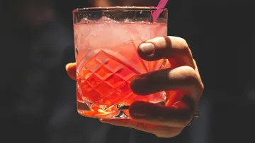 A glass of pink drink is held in the hand.