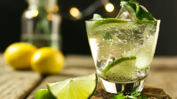 Glas mit Getränk und Limettenstücken auf Holzuntergrund.