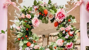 A wreath of flowers hangs decoratively on the window of a shop.