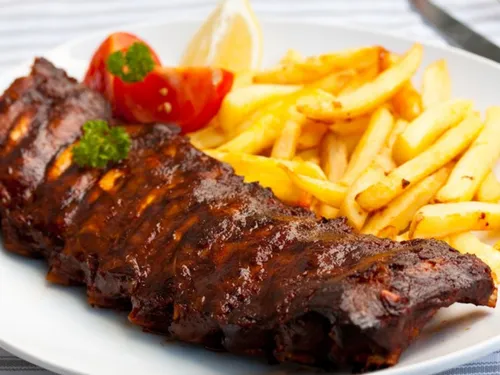 Gegrillte Rippchen, serviert mit Pommes frites und Zitrone.