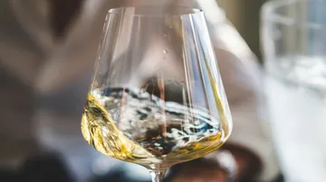 Glass with white wine swirling, water visible in the background.