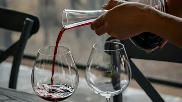 Red wine is poured from a carafe into wine glasses.