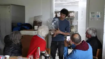 Man shows something, viewers watch in a room.